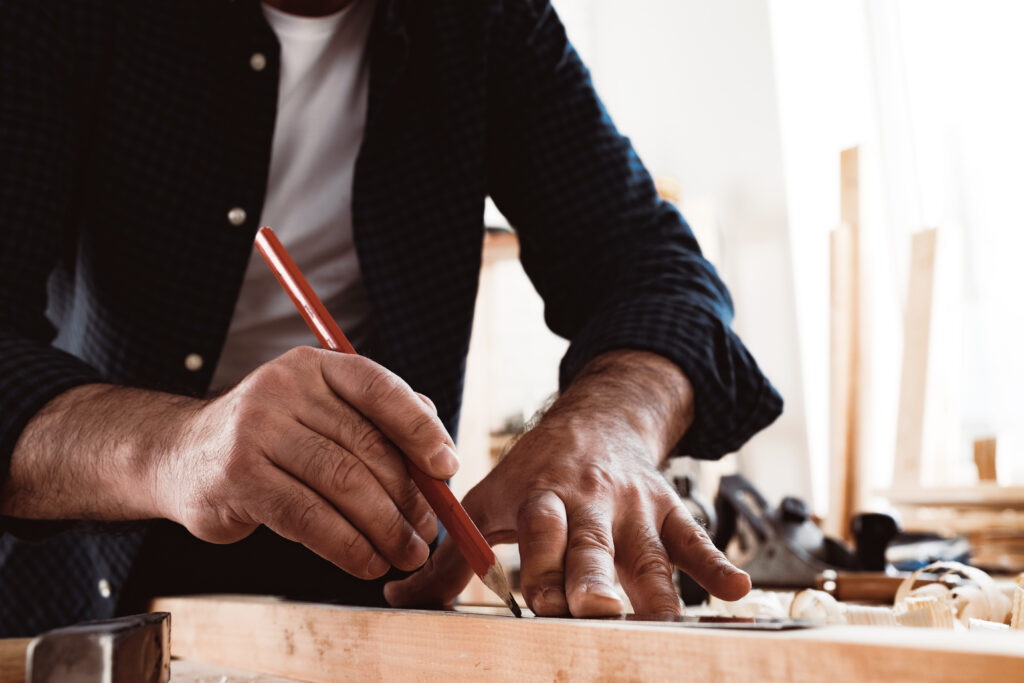 carpenter makes pencil marks on a wood plank